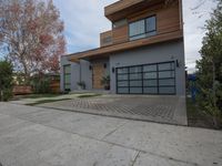 two garages are adjacent each other on the sidewalk near a house with a tree