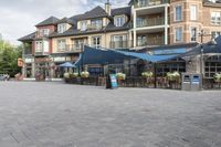 the front view of some very pretty restaurants on a street corner in canada, with blue umbrellas over tables