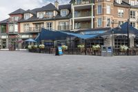 the front view of some very pretty restaurants on a street corner in canada, with blue umbrellas over tables