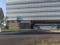 a road going by a very large building with glass walls on top of it near the grass