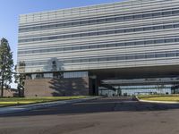 a road going by a very large building with glass walls on top of it near the grass