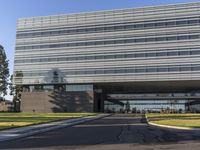 a road going by a very large building with glass walls on top of it near the grass