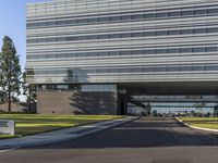 a road going by a very large building with glass walls on top of it near the grass