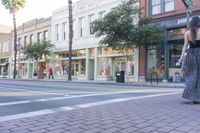 woman standing on sidewalk next to brick roadway and looking out the window of building across road from store