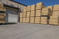 stack of wood pallets by warehouse door in factory yard area of business facility at edge of field