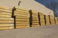 large bunches of lumber stacked outside a building with blue sky in the background by some other wood and lumber on a street