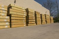 large bunches of lumber stacked outside a building with blue sky in the background by some other wood and lumber on a street