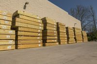 large bunches of lumber stacked outside a building with blue sky in the background by some other wood and lumber on a street