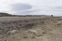 a truck drives on dirt, with rocks and grass surrounding it, in the daytime