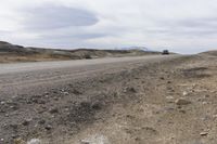 a truck drives on dirt, with rocks and grass surrounding it, in the daytime