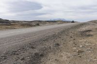 a truck drives on dirt, with rocks and grass surrounding it, in the daytime