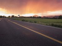 an empty highway in the open field at sunset with sun set in the distance behind it