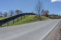 a motorcycle is riding down a rural road in front of a fence and green hill