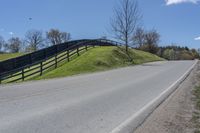 a motorcycle is riding down a rural road in front of a fence and green hill