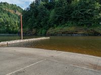 the pier at the river is empty, next to some trees and a hill in the background