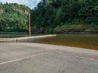 the pier at the river is empty, next to some trees and a hill in the background