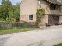 a brown brick building with wooden doors in the grass near a street corner with a bench and picnic table