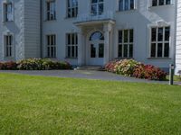 a lawn area in front of a white, four - story building with red flowers