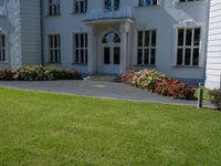 a lawn area in front of a white, four - story building with red flowers