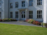 a lawn area in front of a white, four - story building with red flowers