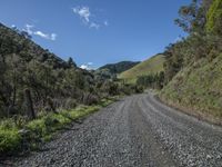 a gravel road going up the side of a mountain near some green hills in a valley