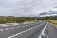 a road with white lines next to a mountain under a cloudy sky on the side of a highway