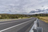 a road with white lines next to a mountain under a cloudy sky on the side of a highway