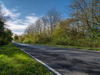 an empty road with the sky in the background and trees in the foreground and grass to the right