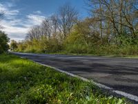 an empty road with the sky in the background and trees in the foreground and grass to the right