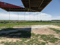 a picture of a glass pavilion over looking a farm field with a sky background and some cars