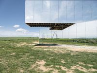 a mirrored photo taken over a grassy field near a metal object in the air, against a bright blue sky