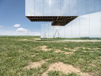 a mirrored photo taken over a grassy field near a metal object in the air, against a bright blue sky