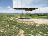 a mirrored photo taken over a grassy field near a metal object in the air, against a bright blue sky