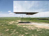 a mirrored photo taken over a grassy field near a metal object in the air, against a bright blue sky