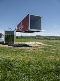 the two shipping containers are being held in the air by a craned pole while green grass and truck in the background