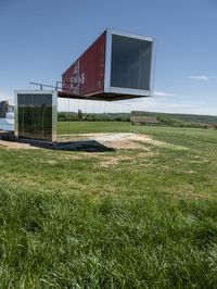 the two shipping containers are being held in the air by a craned pole while green grass and truck in the background