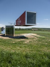 the two shipping containers are being held in the air by a craned pole while green grass and truck in the background