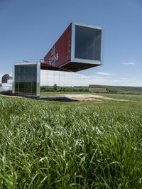 the two shipping containers are being held in the air by a craned pole while green grass and truck in the background