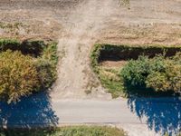 an aerial shot showing a farmer walking down the road in front of his crops and dirt area