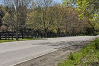 a paved road with a fenced off street beside it with some trees and grass