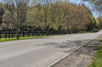 a paved road with a fenced off street beside it with some trees and grass