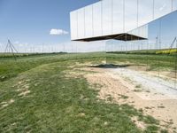 a mirror shaped sculpture is surrounded by grass and power lines and wind turbines on a clear day