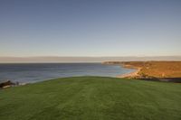 a man sits on the grass with a laptop on the golf course at the ocean's edge