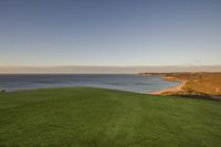 a man sits on the grass with a laptop on the golf course at the ocean's edge