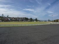 a road in front of a large field of grass with houses in the distance on top of it