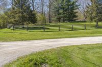 the road is paved with dirt by the fence in this country setting, and a long wooden fence lines a dirt trail