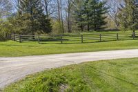 the road is paved with dirt by the fence in this country setting, and a long wooden fence lines a dirt trail