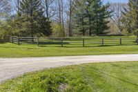 the road is paved with dirt by the fence in this country setting, and a long wooden fence lines a dirt trail