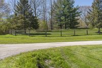 the road is paved with dirt by the fence in this country setting, and a long wooden fence lines a dirt trail