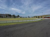 the view from the side of a road looking over to a grassy field and field house